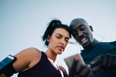 Low angle view of sportsman showing mobile phone to female athlete while standing outdoors - MASF09922