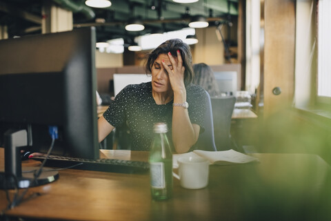 Müde Geschäftsfrau mit Kopf in der Hand sitzt am Computer Schreibtisch im Büro, lizenzfreies Stockfoto