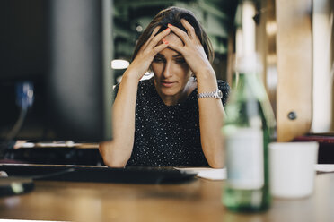 Frustrierte Computerprogrammiererin mit dem Kopf in den Händen am Bürotisch - MASF09929