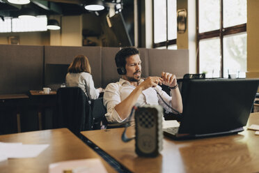 Creative businessman wearing headphones while video conferencing on laptop in office - MASF09932