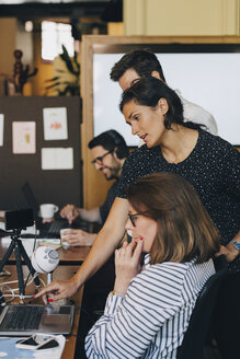 Mittlere erwachsene Geschäftsfrau, die mit ihrem Team über einem Laptop im Büro diskutiert - MASF09949