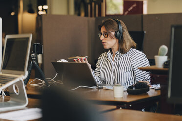 Mature businesswoman wearing headphones while talking on mobile phone in office - MASF09951