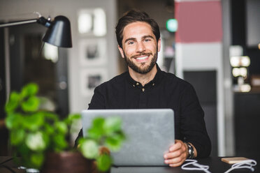 Portrait of confident businessman sitting at desk in creative office - MASF09966