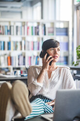 Kreative Geschäftsfrau, die mit ihrem Handy telefoniert, während sie sich am Schreibtisch im Büro entspannt - MASF09976