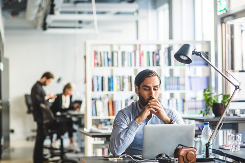 Besorgter Geschäftsmann schaut auf seinen Laptop, während er im Büro sitzt, lizenzfreies Stockfoto