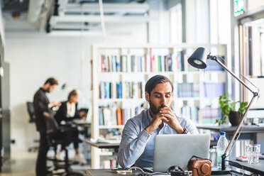 Worried businessman looking at laptop while sitting in office - MASF09982