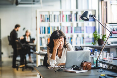 Tired businesswoman leaning by laptop on desk in creative office - MASF09987