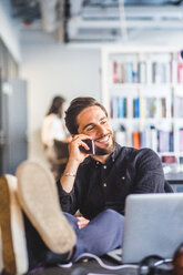 Geschäftsmann, der mit seinem Handy telefoniert, während er sich am Schreibtisch im Büro entspannt - MASF09989