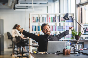 Businessman sitting with arms outstretched at desk in office - MASF09993