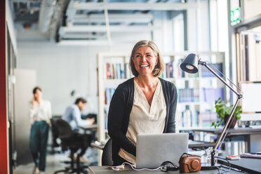 Happy creative businesswoman looking away while standing at desk in office - MASF10002