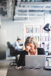 Tired businesswoman with laptop at desk in creative office - MASF10003