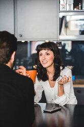 Geschäftsfrau lächelt im Gespräch mit einem männlichen Kollegen am Tisch im Büro - MASF10010