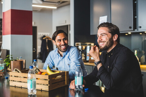 Männliche Kollegen, die lächelnd am Tisch im Büro sitzen, lizenzfreies Stockfoto
