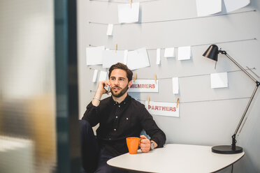 Creative businessman talking on mobile phone while sitting at desk in office - MASF10021