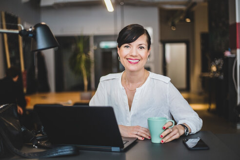 Porträt einer selbstbewussten Geschäftsfrau, die eine Kaffeetasse hält, während sie am Schreibtisch im Büro sitzt - MASF10024