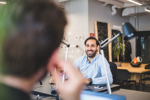 Geschäftsmann lächelnd mit Blick auf einen männlichen Kollegen im Büro, lizenzfreies Stockfoto