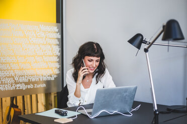 Geschäftsfrau lächelt, während sie am Schreibtisch in einem kreativen Büro über ein Mobiltelefon spricht - MASF10044