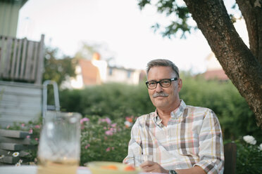 Portrait of smiling senior man sitting at table in backyard - MASF10074