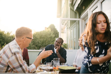 Mehrgenerationenfamilie unterhält sich beim Mittagessen am Tisch auf der Veranda - MASF10081