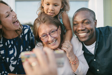 Ausgeschnittenes Bild eines Mannes, der einer glücklichen Familie auf einer Veranda sein Handy zeigt - MASF10086