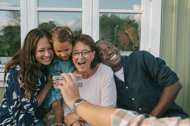 Ausgeschnittenes Bild eines Mannes, der einer fröhlichen Familie auf einer Veranda sein Handy zeigt - MASF10087