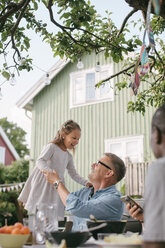Verspieltes Mädchen, das bei seinem Großvater im Hinterhof steht, während einer Gartenparty - MASF10100