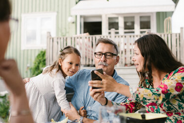 Mid adult woman showing mobile phone to family while sitting in backyard - MASF10101