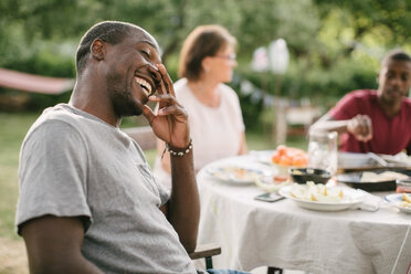 Mittlerer erwachsener Mann lächelt, während er bei einer Gartenparty am Tisch sitzt - MASF10107