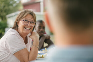 Lächelnde ältere Frau, die wegschaut, während sie bei einer Gartenparty am Tisch sitzt - MASF10109