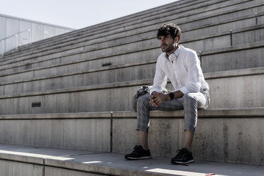 Junger Mann mit Kopfhörern sitzt auf einer Treppe im Freien - GIOF04823