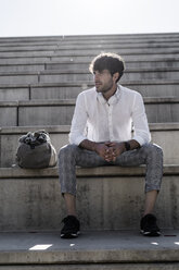 Junger Mann mit Kopfhörern sitzt auf einer Treppe im Freien - GIOF04824