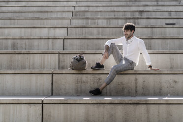 Young man with headphones sitting on stairs outdoors - GIOF04825