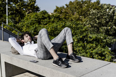 Junger Mann liegt auf einer Bank im Freien und entspannt sich - GIOF04828
