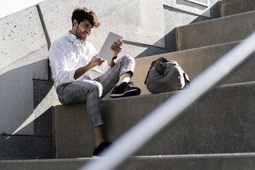 Lächelnder junger Mann sitzt auf einer Treppe im Freien und benutzt ein Tablet - GIOF04836