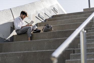 Smiling young man sitting on stairs outdoors using tablet - GIOF04837