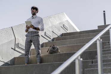 Junger Mann steht auf einer Treppe im Freien und hält ein Tablet - GIOF04838