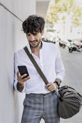 Junger Mann mit Tasche und Mobiltelefon in der Stadt - GIOF04856