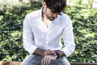Junger Mann sitzt im Freien und benutzt eine Smartwatch - GIOF04860