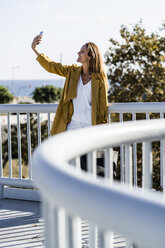 Lächelnde Frau macht ein Selfie auf einer Brücke - GIOF04886