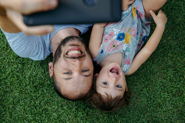 Happy father and daughter taking a selfie with cellphone on green grass - GEMF02634