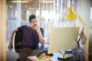 Kreativer Geschäftsmann, der auf einen Computerbildschirm schaut, während er im Büro sitzt - MASF10153
