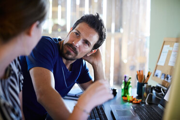 Geschäftsfrau im Gespräch mit einem männlichen Kollegen am Computer in einem kreativen Büro - MASF10157