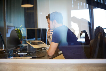 Geschäftsmann sitzt am Computer Schreibtisch durch Glas im Büro gesehen - MASF10158