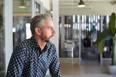 Thoughtful mature businessman looking away while sitting in creative office - MASF10164