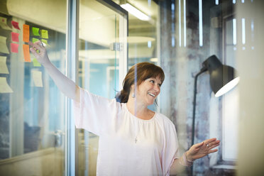 Smiling businesswoman discussing while pointing at sticky notes in creative office - MASF10193