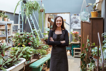 Portrait of smiling female owner standing with arms crossed by potted plants at store - MASF10238