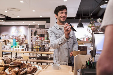 Male customer showing mobile phone while doing contactless payment to cashier at cafe - MASF10240