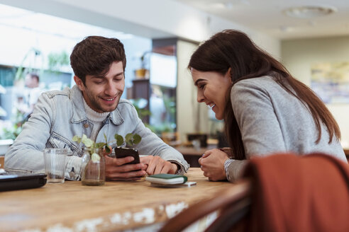 Lächelnde männliche und weibliche Freunde schauen in einem Café auf ihr Smartphone - MASF10242