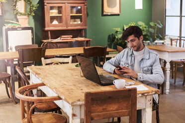 Male customer using smart phone and laptop at table in cafe - MASF10243