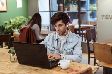Junger Mann, der einen Laptop benutzt, während er am Tisch in einem Café Kaffee trinkt - MASF10245